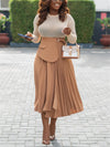 Elegant woman wearing a pleated high waist split skirt, stylish top, and holding a handbag, walking on a city pavement.