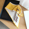 Small yellow and white silky scarf with playful designs, elegantly displayed on a wooden surface.