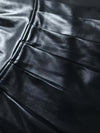 Close-up of the pleats on an elegant women's black PU leather skirt, showcasing glossy texture and high-quality material.