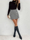 Woman in a black long-sleeve top and plaid asymmetrical skirt, styled with knee-high black boots for a chic look.