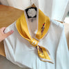 Elegant yellow silky scarf with playful designs, styled on a white blouse, perfect for versatile fashion looks.