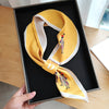 Small long silk scarf in yellow with elegant design, displayed in a box, perfect stylish accessory for women.